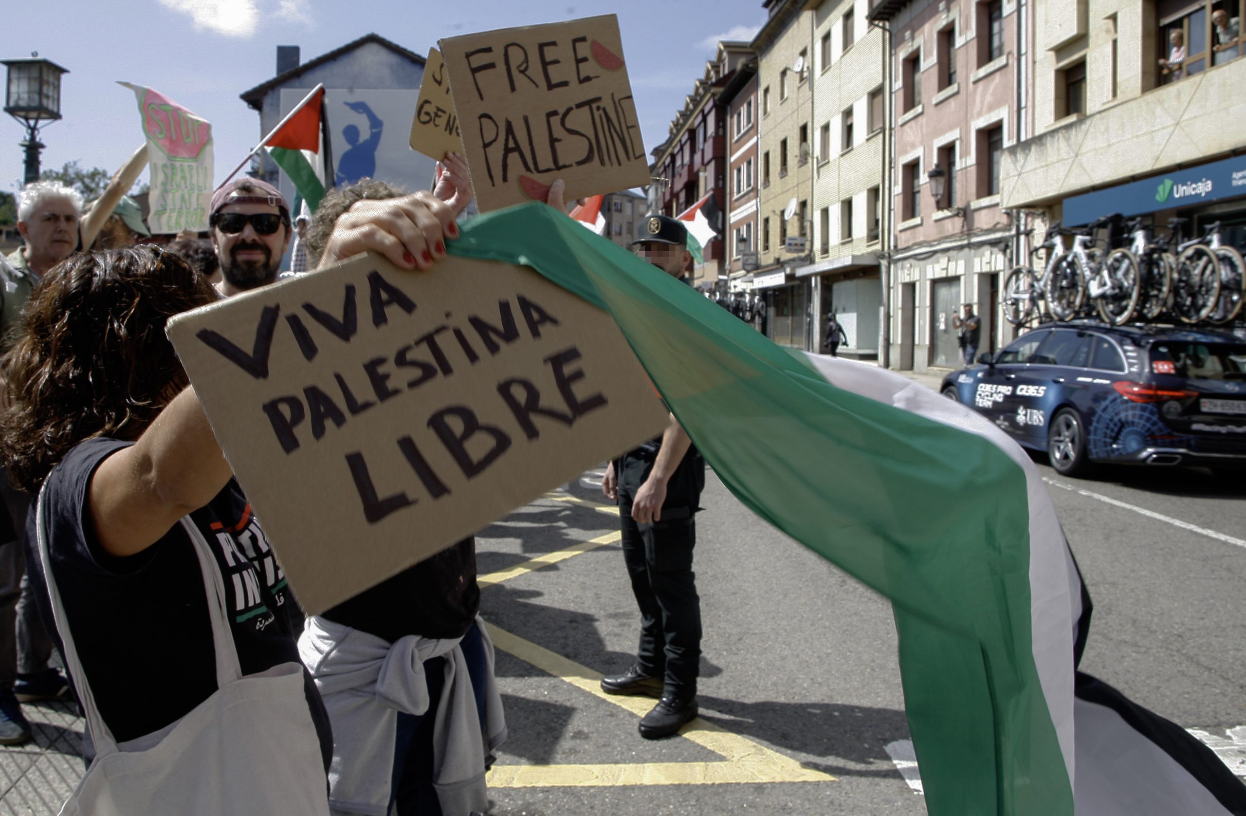 Decenas de personas con banderas de Palestina condenan el genocidio en Gaza al paso de los corredores por la localidad asturiana de Nava, durante la etapa 13 de la Vuelta Ciclista a España 2025 disputada entre el Cabezón de la Sal, y L'Angliru, de 202,7km de recorrido, este viernes. EFE / Juan González.