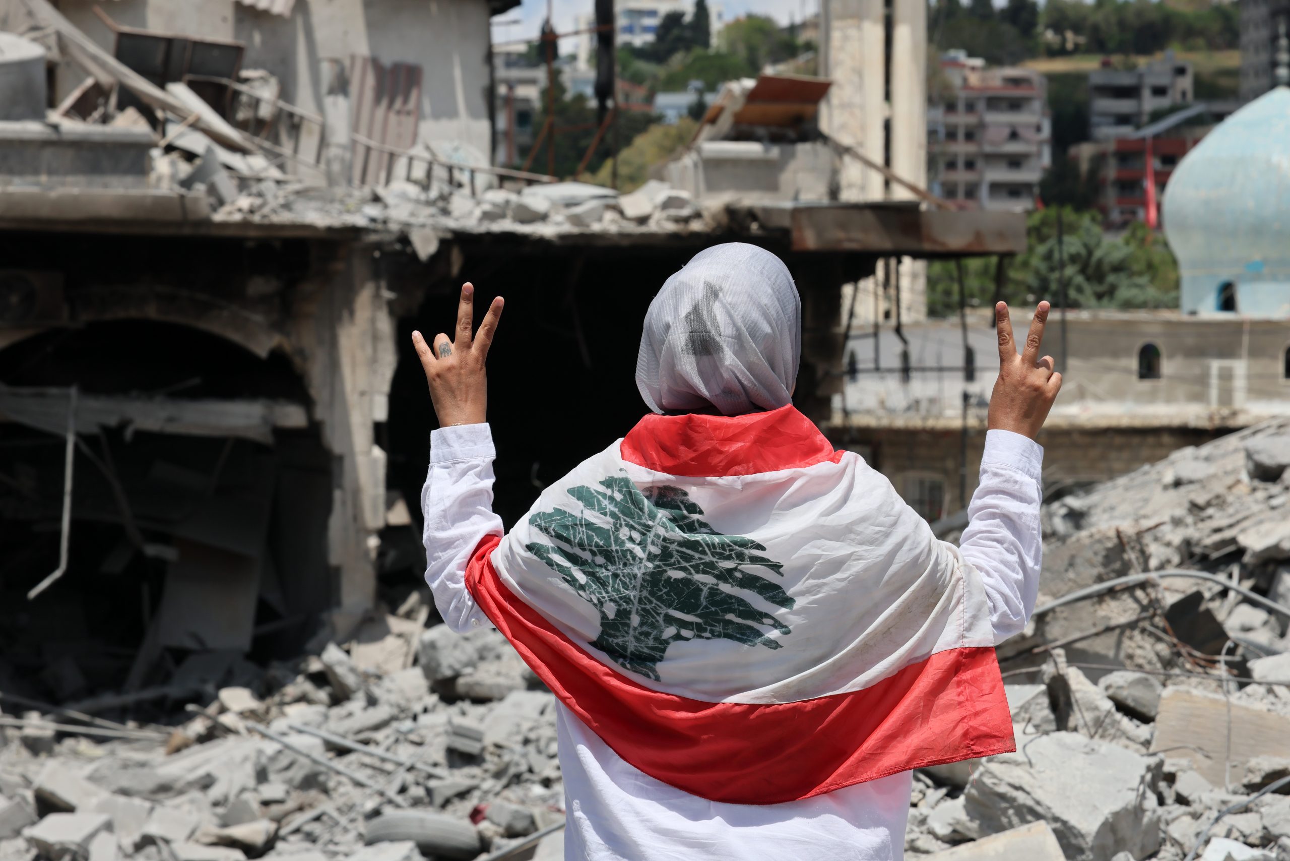 NABATIEH (Líbano), 15/06/2026.- Una mujer hace el gesto de la victoria junto a unos edificios destruidos tras los ataques israelíes contra el histórico mercado antiguo de la localidad de Nabatieh, en el sur del Líbano, el 15 de junio de 2026, tras el anuncio de un acuerdo marco preliminar, mediado por Estados Unidos e Irán, para poner fin a las hostilidades militares en la región y levantar el bloqueo naval del estrecho de Ormuz. (Líbano) EFE/EPA/WAEL HAMZEH